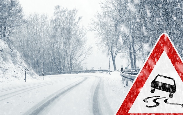 Ice and snow covered road with a slippery drive caution sign.