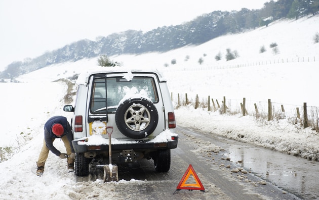 Man changing his car tires on the road in winter.